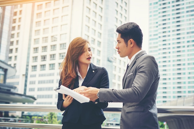 Business man pointing at document with smile and discussing something with her coworker while standing in front of office.