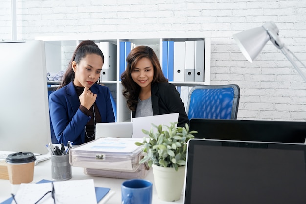 Two Asian female colleagues sitting together in office and looking at document