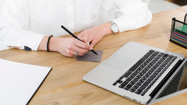 Close-up of businesswoman writing on adhesive note with pen over the wooden desk