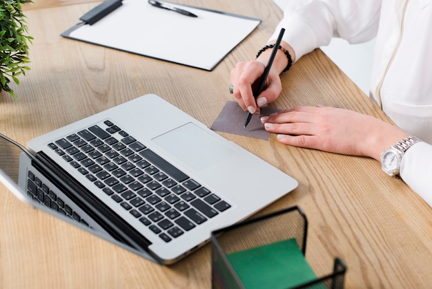 Young businesswoman writing on note with pen over the wooden desk with laptop